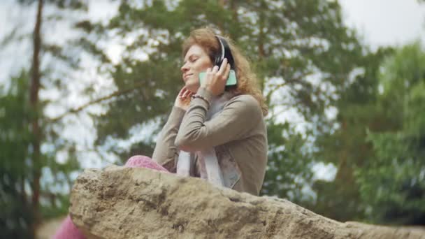 Een Vrouw Luistert Naar Muziek Hoofdtelefoon Ontspant Rotsen Een Prachtig — Stockvideo