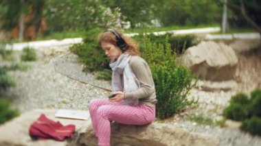 Bir kadın kulaklıklar müzik dinler, güzel bir yeşil park buzlu rahatlatır. Botanik Bahçesi genç bir çok yıllık kadın müzik dinliyor. Açık havada teknoloji