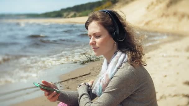 Женщина слушает музыку в наушниках, расслабляется и танцует на берегу морской реки. Технологии на открытом воздухе — стоковое видео