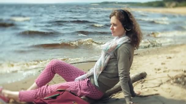 Una mujer escucha música en los auriculares, se relaja y baila en la orilla del río del mar del océano. Tecnología al aire libre — Vídeos de Stock