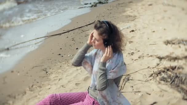 Μια γυναίκα ακούει μουσική με ακουστικά, χαλαρώνει και χορούς στην όχθη του ποταμού στη θάλασσα, του ωκεανού. Τεχνολογία στην ύπαιθρο — Αρχείο Βίντεο