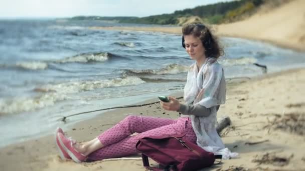 一个女人听音乐的耳机, 放松和舞蹈在岸边的海洋河。开放空气中的技术 — 图库视频影像