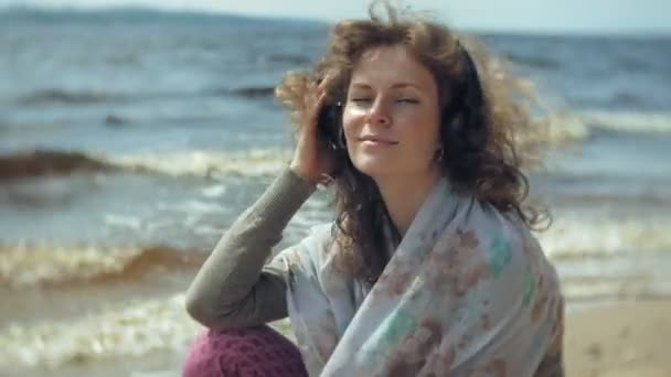 Vrouw luistert naar muziek op de hoofdtelefoon, ontspant en danst op de oever van de zee van de Oceaan. Technologie in de open lucht — Stockvideo