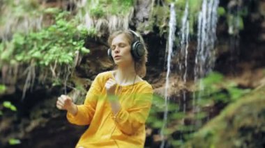 geniş LCD ekranı kulaklık müzik dinlemek bir şelale yakınındaki genç şık güzel kadın.