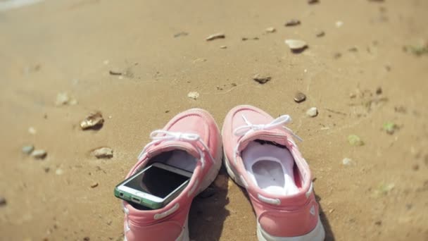 Chaussures d'été sur la plage. dans le fond d'une fille marchant et dansant sur le sable — Video