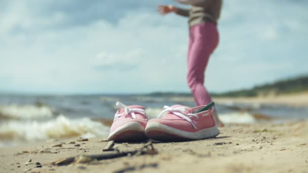 Sommerschuhe am Strand. im Hintergrund ein Mädchen, das auf dem Sand geht und tanzt — Stockvideo
