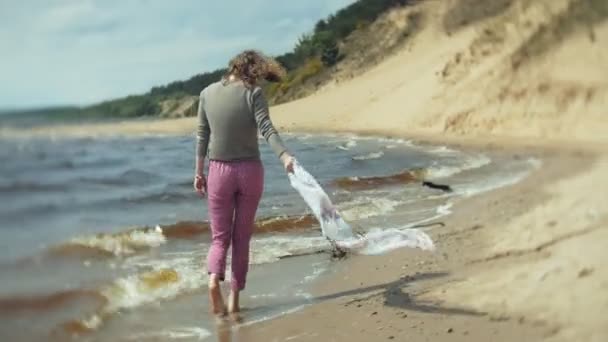 En kvinna lyssnar på musik i hörlurar, slappnar av och dansar på stranden av floden havet över havet. Teknik utomhus — Stockvideo