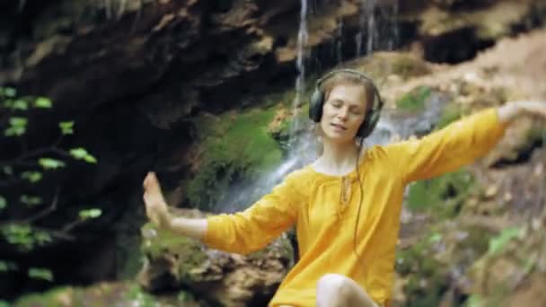 Mladé stylové krásná žena, poblíž vodopádu poslechu hudby ve velkém monitoru sluchátka. — Stock video
