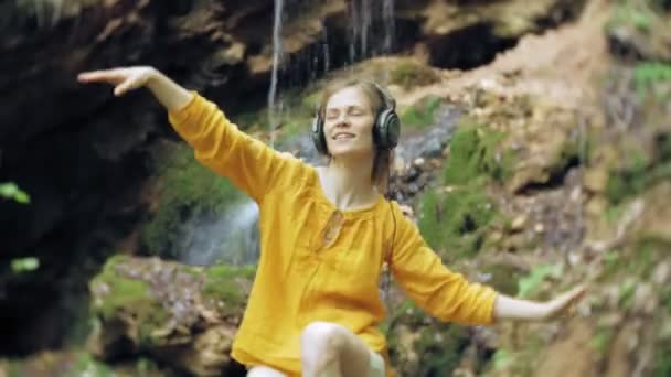 Mladé stylové krásná žena, poblíž vodopádu poslechu hudby ve velkém monitoru sluchátka. — Stock video