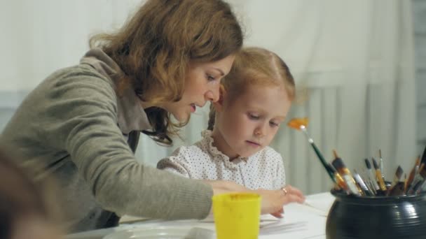 Kinder sitzen zusammen am Tisch im Klassenzimmer und zeichnen mit den Fingern und malen. mit ihnen ihre junge und schöne Lehrerin. — Stockvideo