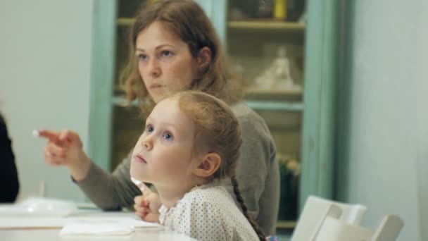 Le bambine si siedono insieme a tavola in classe e disegnano con le dita e dipingono. Con loro la loro giovane e bella maestra . — Video Stock