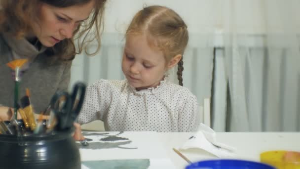 Children girls sit together at the table in the classroom and drawing with their fingers and paint. With them their young and beautiful teacher. — Stock Video