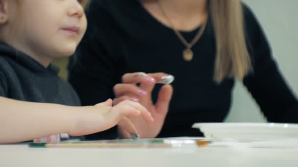 子供女の子は教室と自分の指とペイントで図面内のテーブルに一緒に座る。彼らと彼らの若くて美しい先生. — ストック動画