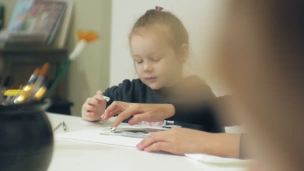 Las niñas se sientan juntas a la mesa en el aula y dibujan con los dedos y pintan. Con ellos su joven y hermosa maestra . — Vídeos de Stock