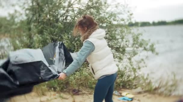 Familia de niños y madres reúnen una tienda de campaña turística en la orilla del río del mar — Vídeos de Stock