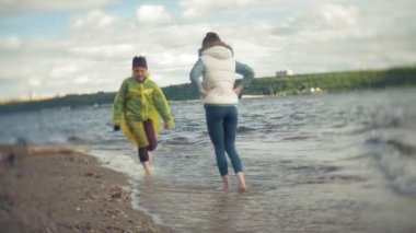 Anne oğlunu yağmurluk ile çalış ve sahilde deniz aşağı çalışır