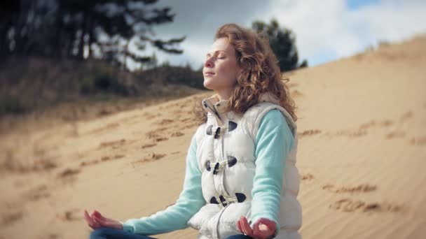 Kvinna sitter i en lotus yogaställning på sanden nära vattnet — Stockvideo