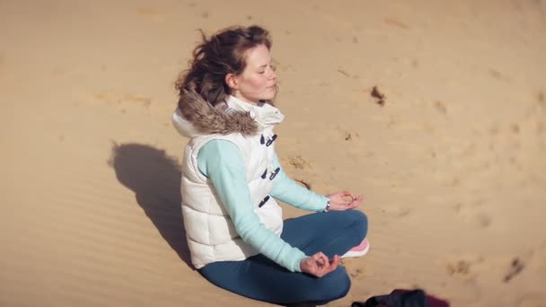 Woman sitting in a lotus yoga pose on the sand near the water — Stock Video