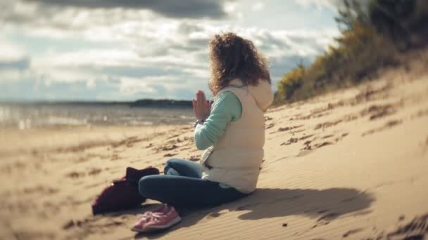 Γυναίκα που κάθεται σε στάση λωτού γιόγκα στην άμμο κοντά στο νερό — Αρχείο Βίντεο