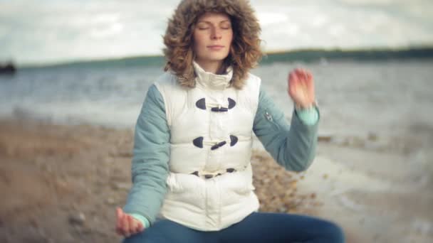 Женщина, сидящая в позе йоги лотоса на песке у воды — стоковое видео