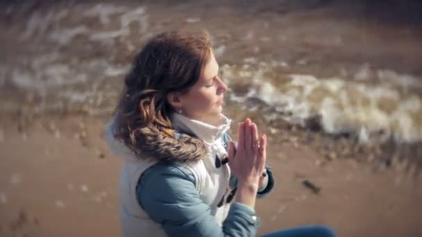 Woman sitting in a lotus yoga pose on the sand near the water — Stock Video