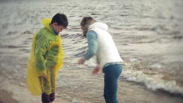 La madre juega con su hijo en un impermeable y corre por el mar en la playa — Vídeos de Stock