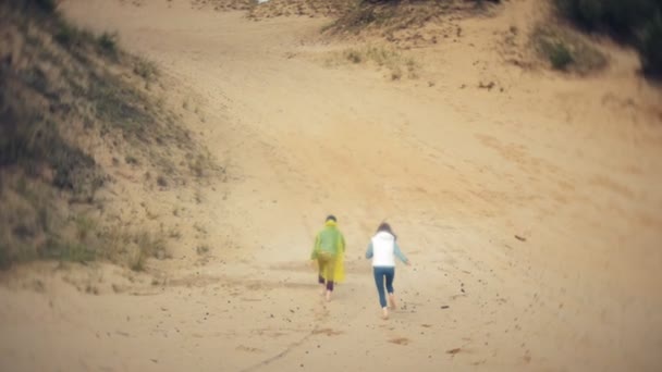 Mamma leker med sin son i en regnrock och rinner längs havet vid stranden — Stockvideo