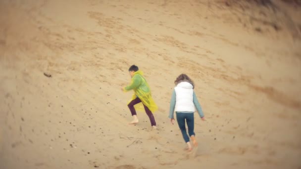 La madre juega con su hijo en un impermeable y corre por el mar en la playa — Vídeo de stock