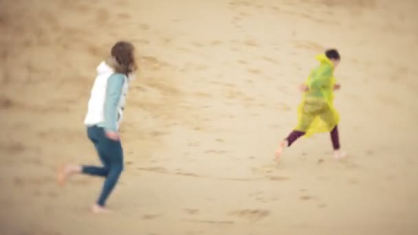 Мать играет со своим сыном в плаще и бежит по морю на пляже — стоковое видео
