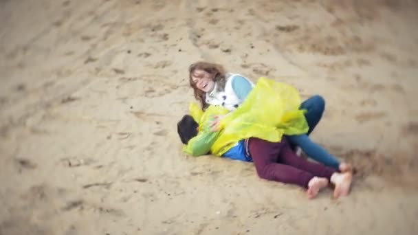 De moeder speelt met haar zoon in een regenjas en vertraagt de zee op het strand — Stockvideo
