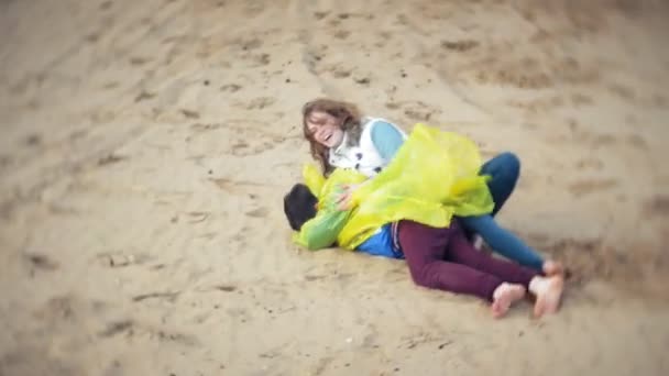 La madre gioca con suo figlio con un impermeabile e corre giù per il mare in spiaggia — Video Stock