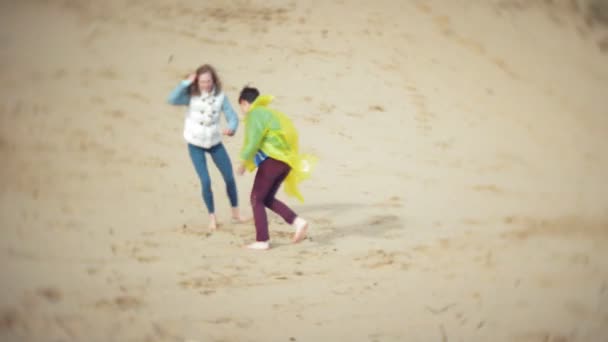母親はレインコートで彼女の息子と遊ぶ、ビーチで海を実行 — ストック動画