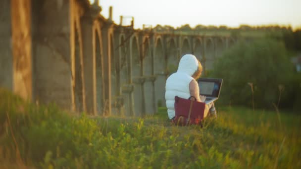 在老式铁路桥梁附近的笔记本电脑工作的年轻妇女. — 图库视频影像