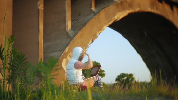 Junge Frau arbeitet an Laptop in der Nähe alter Eisenbahnbrücke. — Stockvideo