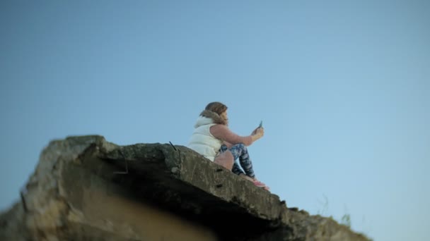Una joven está usando un teléfono inteligente cerca de un viejo puente ferroviario vintage . — Vídeo de stock