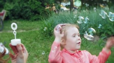 Mutlu anne ve küçük kızı birlikte oynayan açık, üfleme sabun köpüğü, arka bahçesinde üzerinde eğleniyor. Doğa. Güzellik Anne ve çocuk parkı birlikte. Anne ve bebek