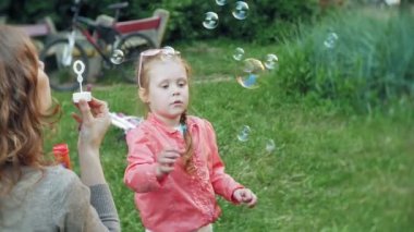 Mutlu anne ve küçük kızı birlikte oynayan açık, üfleme sabun köpüğü, arka bahçesinde üzerinde eğleniyor. Doğa. Güzellik Anne ve çocuk parkı birlikte. Anne ve bebek