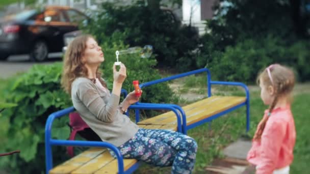 Feliz madre y su pequeña hija jugando juntos al aire libre, soplando burbujas de jabón, divirtiéndose en el patio trasero. Naturaleza. Beauty Mum y su hija en el parque juntas. Mamá y bebé — Vídeo de stock