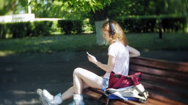 Donna pattinaggio e ascolto di musica sulle cuffie al telefono nel parco — Video Stock