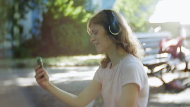 妇女旱冰和听音乐在耳机上的电话在公园4K — 图库视频影像