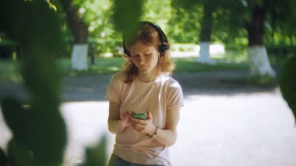 妇女旱冰和听音乐在耳机在电话在公园 — 图库视频影像