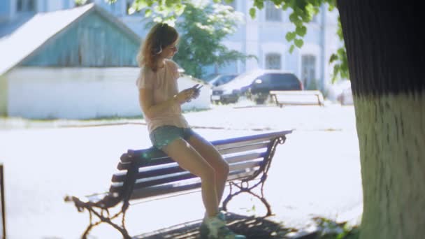 Mujer patinando y escuchando música en los auriculares en el teléfono en el parque — Vídeos de Stock