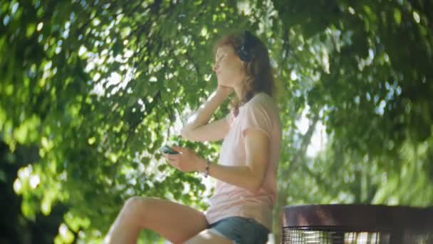 Mujer patinando y escuchando música en los auriculares en el teléfono en el parque — Vídeos de Stock