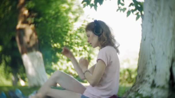 女性ローラーブレードと公園で携帯電話でヘッドフォンで音楽を聴く — ストック動画