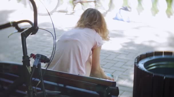 Женщина одевает роликовые коньки сидя на скамейке в парке — стоковое видео