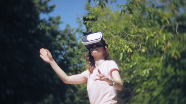 Νεαρή γυναίκα χρησιμοποιεί οθόνη τοποθετείται στο κεφάλι στο πάρκο. Παίζοντας το παιχνίδι χρησιμοποιώντας Vr-κράνος για τα smart phones. Ευτυχισμένο — Αρχείο Βίντεο