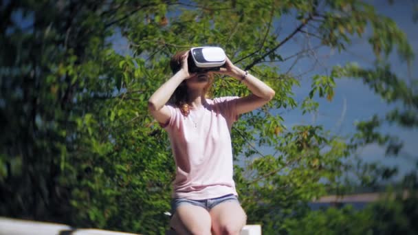 Jonge vrouw maakt gebruik van hoofd gemonteerde display in het park. Spelen spel met behulp van Vr-helm voor slimme telefoons. Gelukkig — Stockvideo