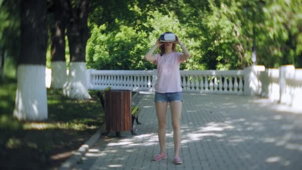 Mujer joven utiliza la pantalla montada en la cabeza en el parque. Jugar a juego con casco VR para teléfonos inteligentes. Feliz. — Vídeos de Stock