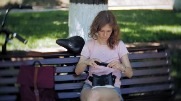 젊은 여자는 공원에서 머리 장착형 디스플레이 사용합니다. 스마트 폰에 대 한 Vr 헬멧을 사용 하 여 재생 게임. 행복 — 비디오