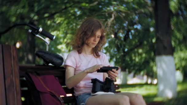 Mujer joven utiliza la pantalla montada en la cabeza en el parque. Jugar a juego con casco VR para teléfonos inteligentes. Feliz. — Vídeos de Stock